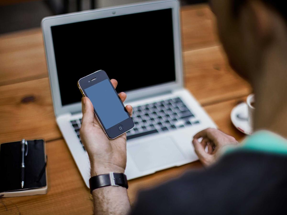 A person exploring AI models on a phone and laptop at a warm wooden desk